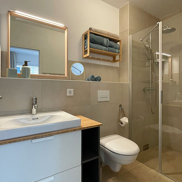 Bad mit Glas-Dusche, Toilette, Keramik-Becken und Spiegel.