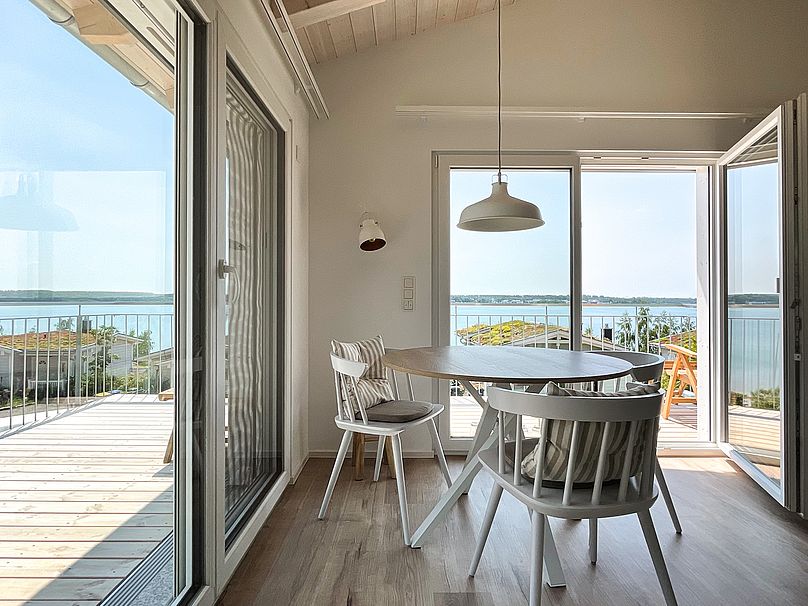 Ess-Tisch mit drei Stühlen im Wohn-Zimmer. Geöffnete Glas-Türen zum Eck-Balkon.