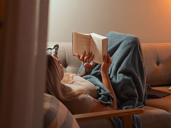 Frau liest in Kuscheldecke auf dem Sofa, © Nicolas Anst